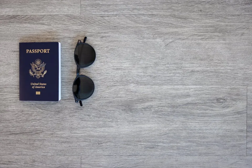 A U.S. passport and a pair of sunglasses on a gray wooden floor