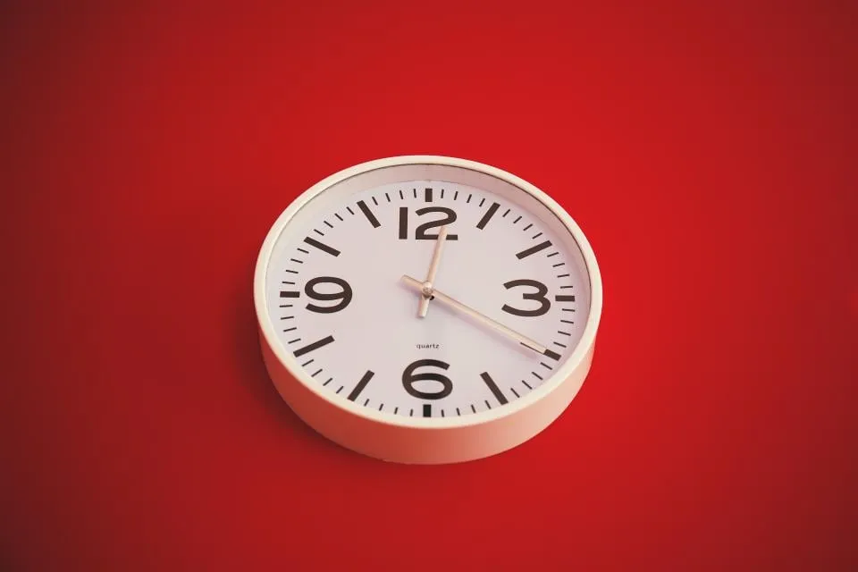 A round white wall clock with black numerals against a plain red background