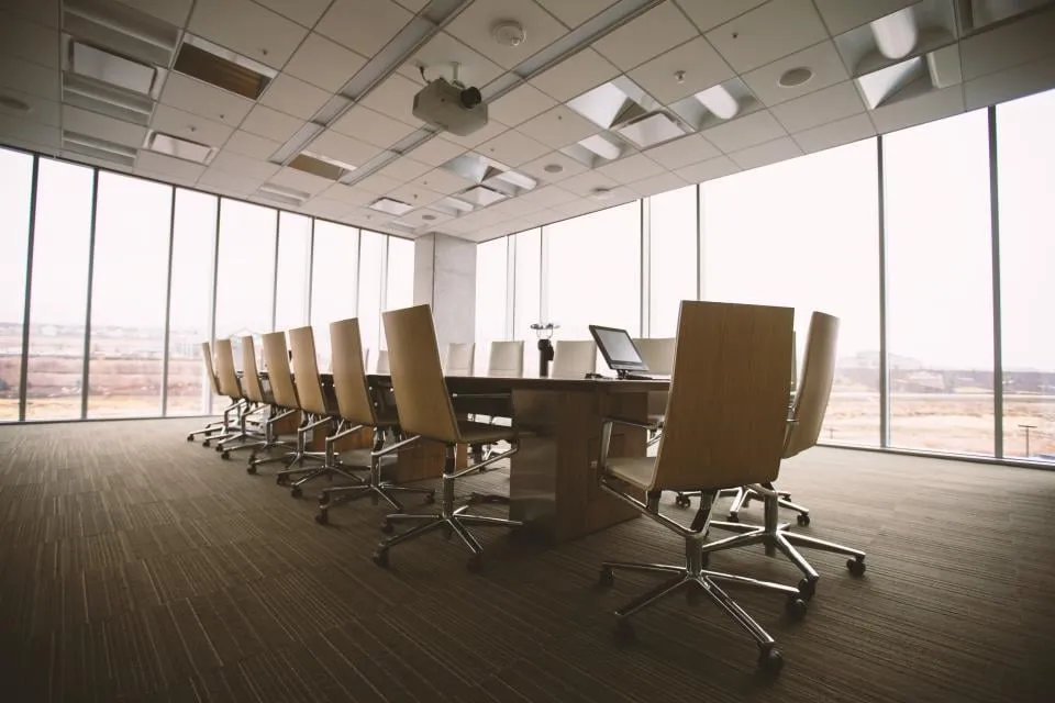 An empty conference room with a long wooden table, leather office chairs and floor-to-ceiling windows