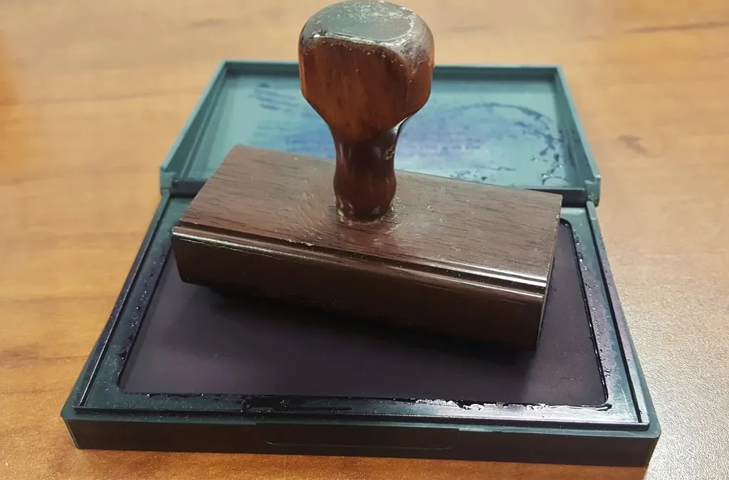 A wooden rubber stamp resting on an open ink pad on a desk