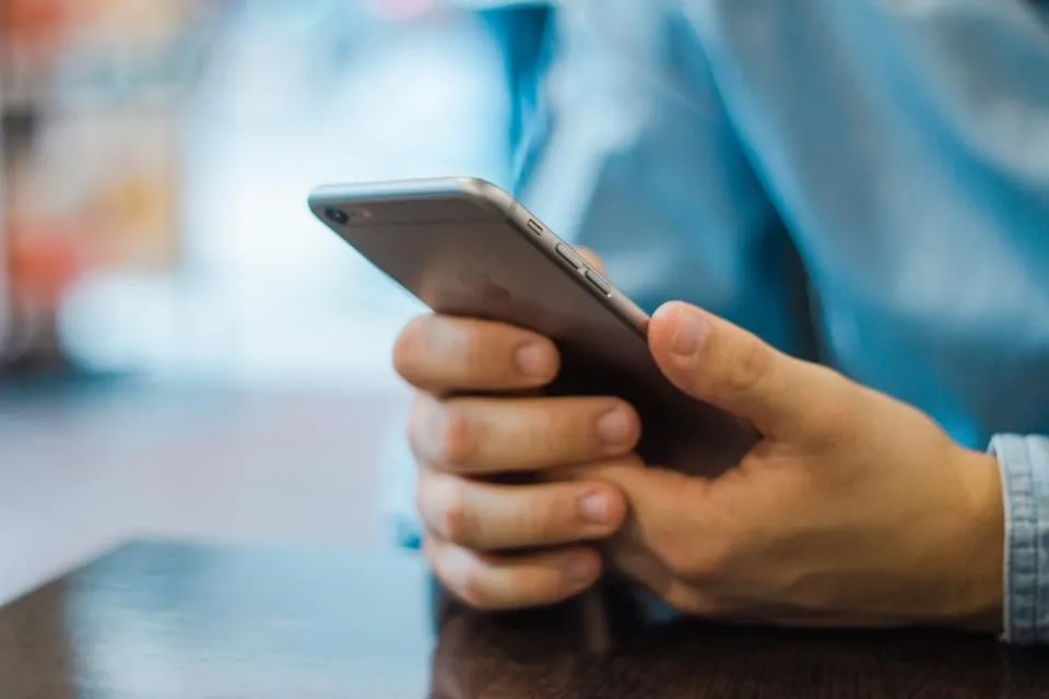 Two hands holding a smartphone over a dark wooden table
