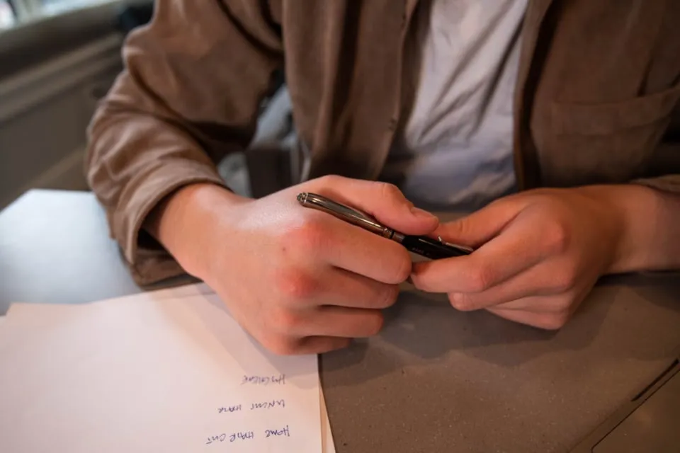 A person's hands holding a pen over a sheet of paper with handwritten notes on a desk