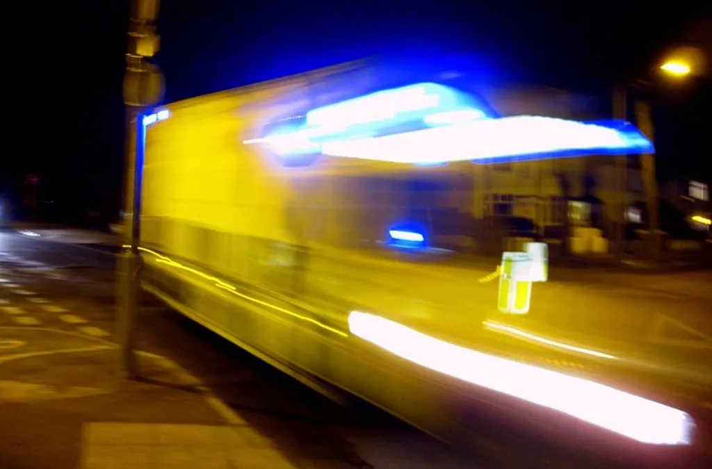 A yellow emergency vehicle with blue lights speeding past at night, blurred by motion