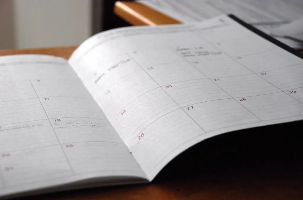 An open monthly planner lying on a wooden desk with the days of the month printed in red