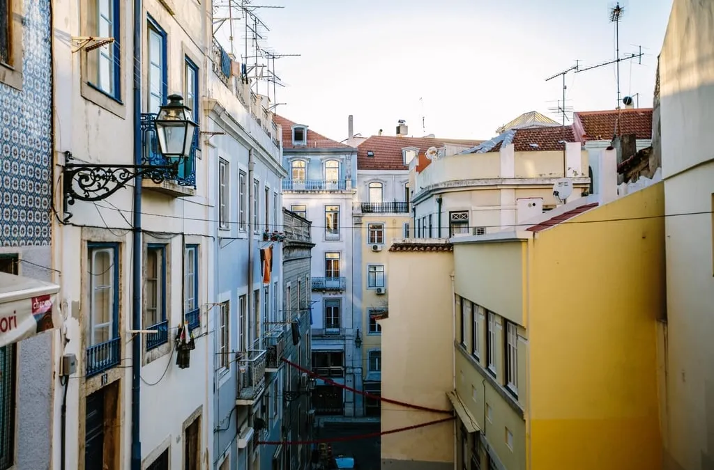 A narrow street of pastel buildings with a tiled facade and an iron lantern in Lisbon