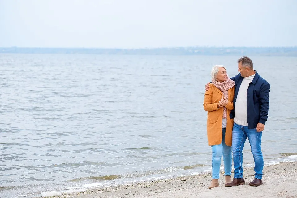 An older couple standing together on a beach by the water