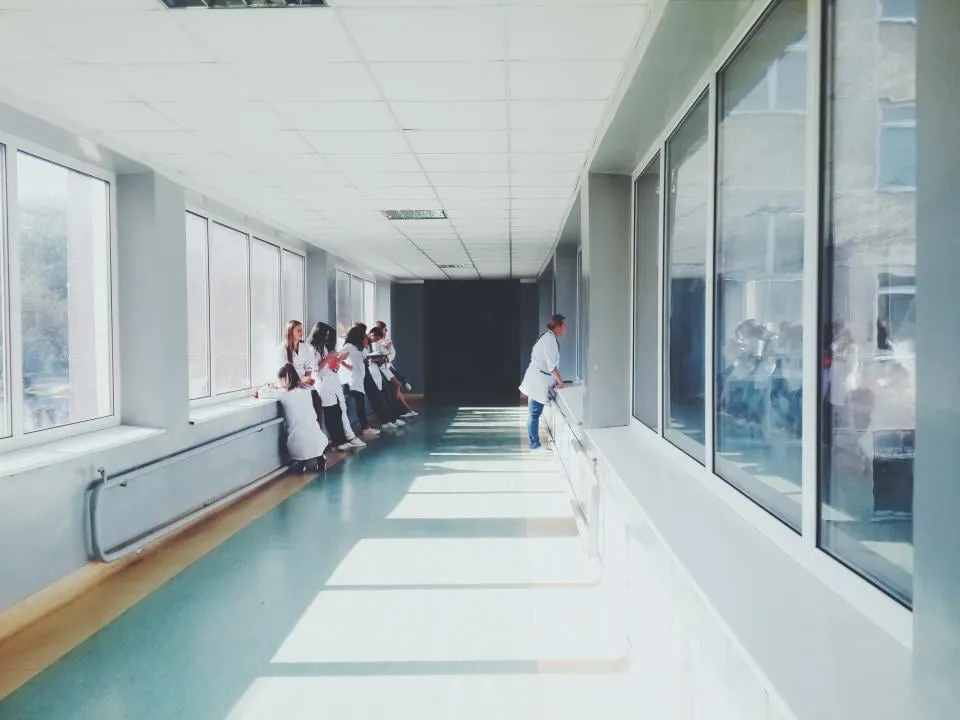 A bright hospital corridor with staff in white coats gathered at the windows