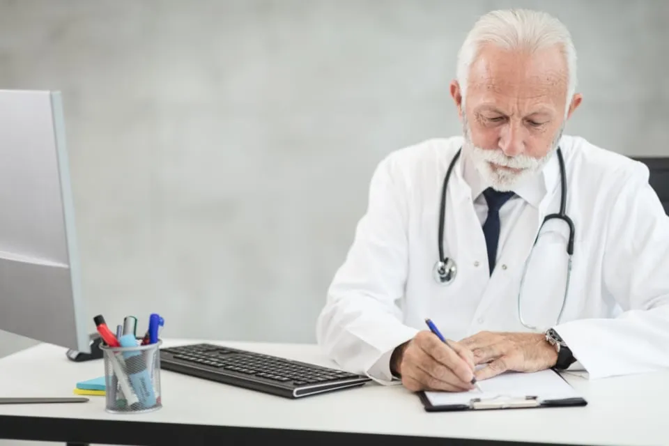 A doctor in a white coat writing notes at a desk