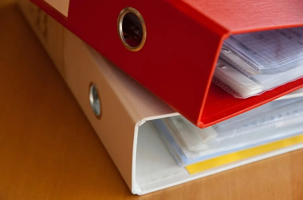 Two stacked office binders, one red and one white, filled with plastic sleeves and papers