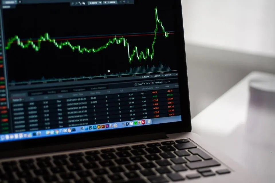 A laptop screen showing a price chart and a table of trades