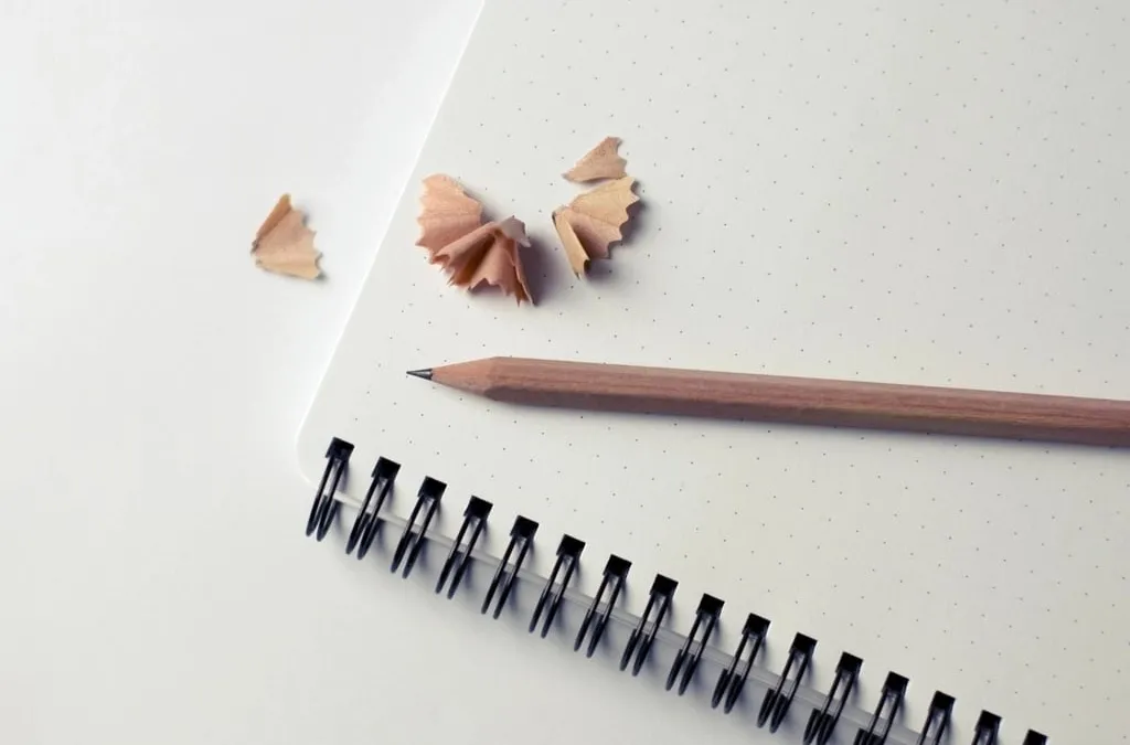 A pencil and wood shavings on the dotted page of a spiral notebook