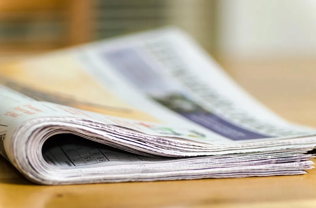 A folded newspaper lying on a wooden table, blurred in the foreground