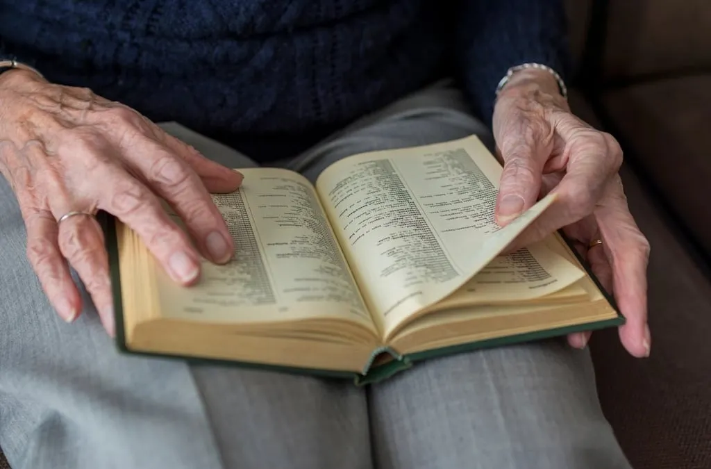 An older person's hands holding an open book on their lap