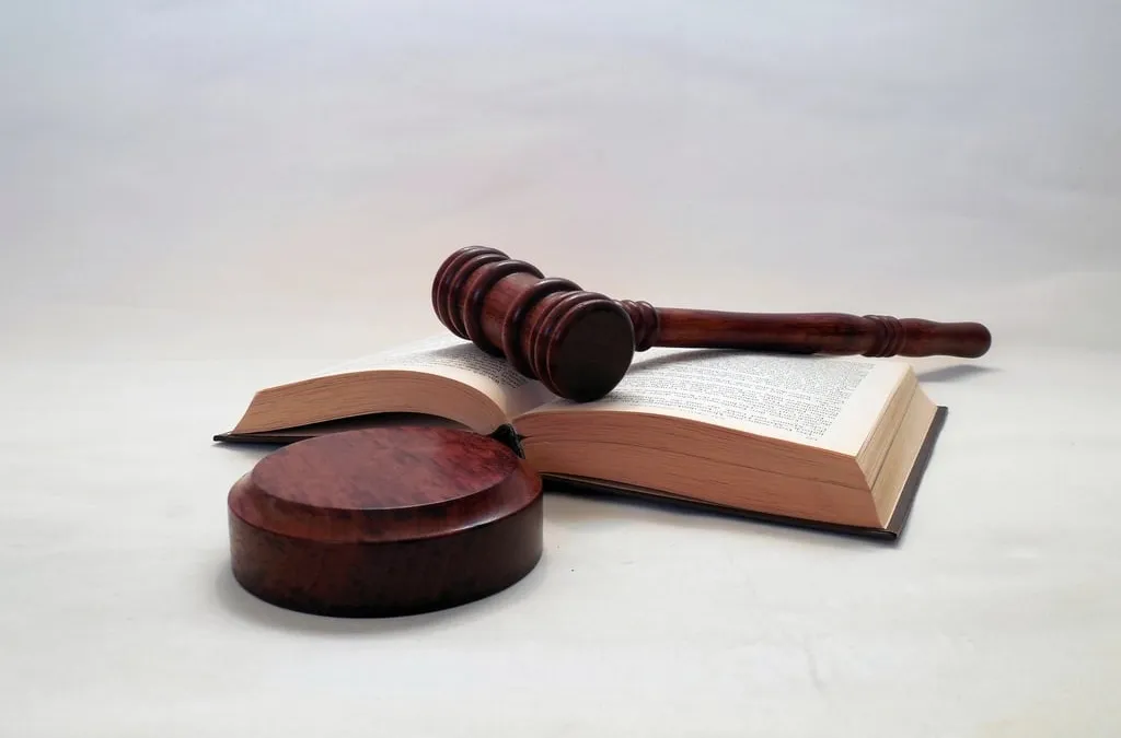 A wooden gavel resting on an open law book beside its sound block