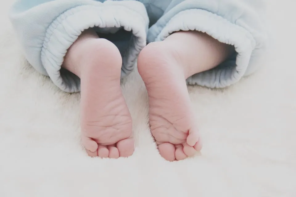 A newborn baby's bare feet resting on a soft white blanket