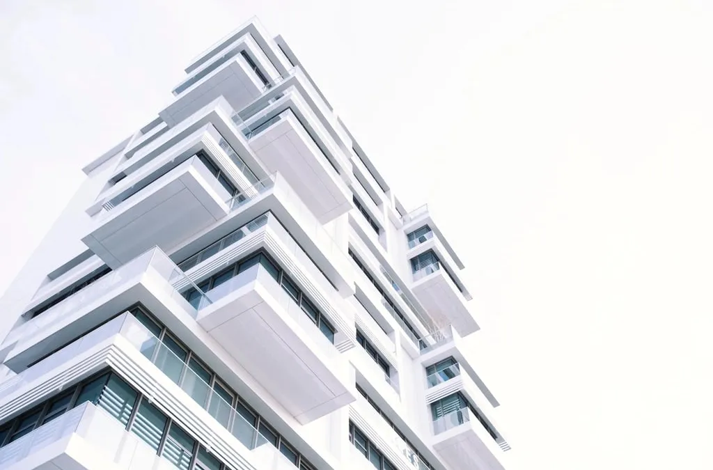 A modern white apartment building with terraces seen from below against a pale sky