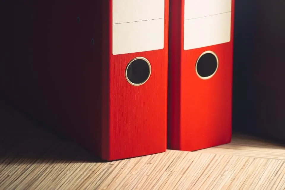Two red office file binders standing on a wooden floor