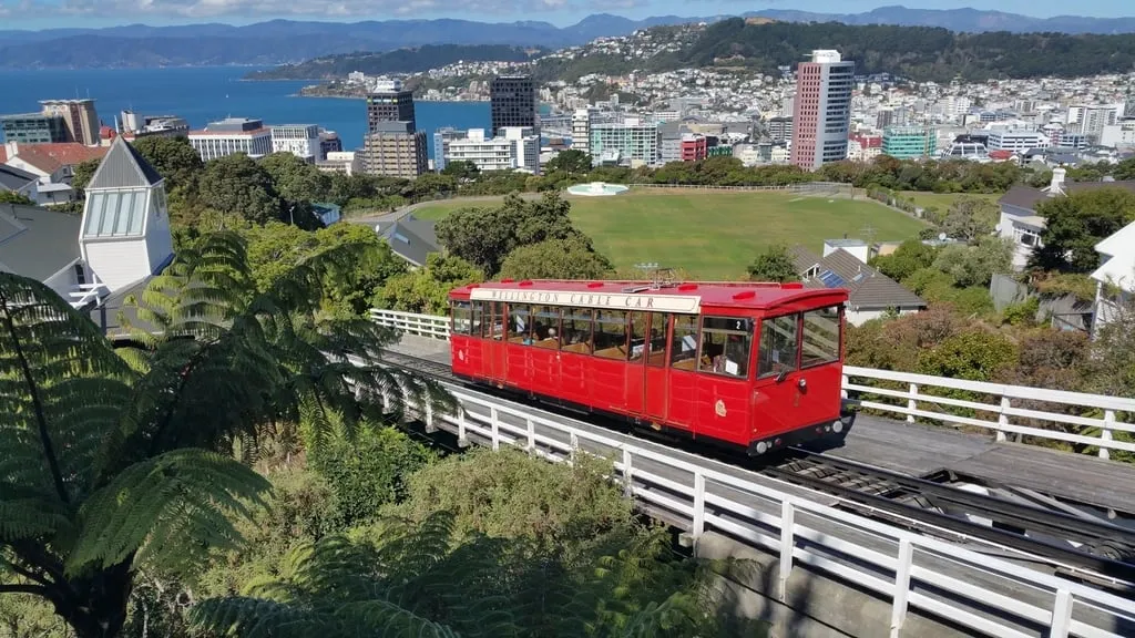 A red cable car climbing a hillside above a city