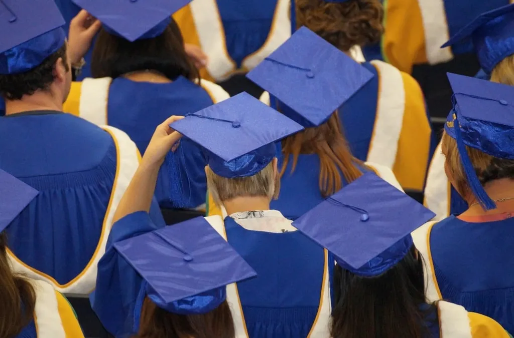 Graduates seen from behind in blue gowns and blue mortarboards at a ceremony