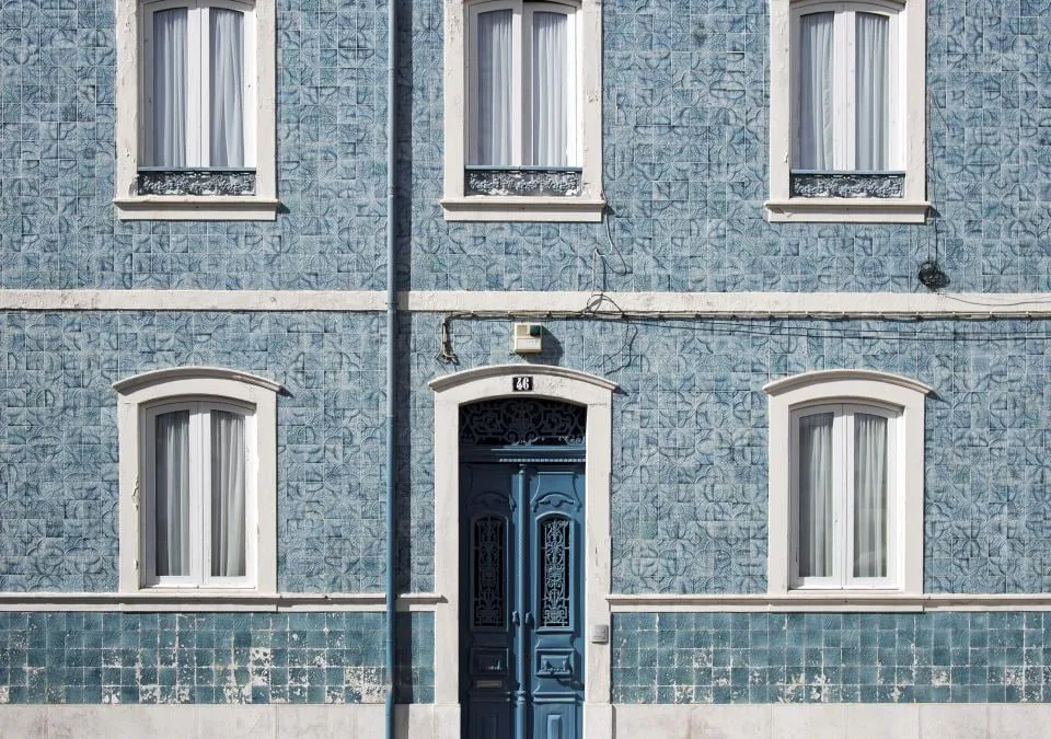A house front covered in blue patterned tiles, with four windows and a blue double door