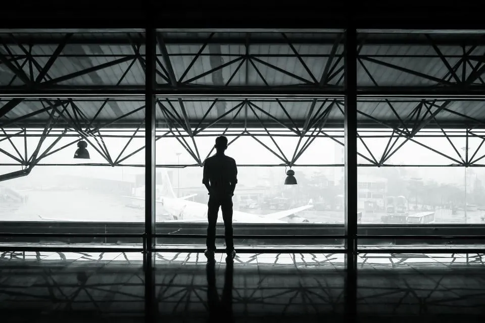 A person seen in silhouette looking out through a large airport window