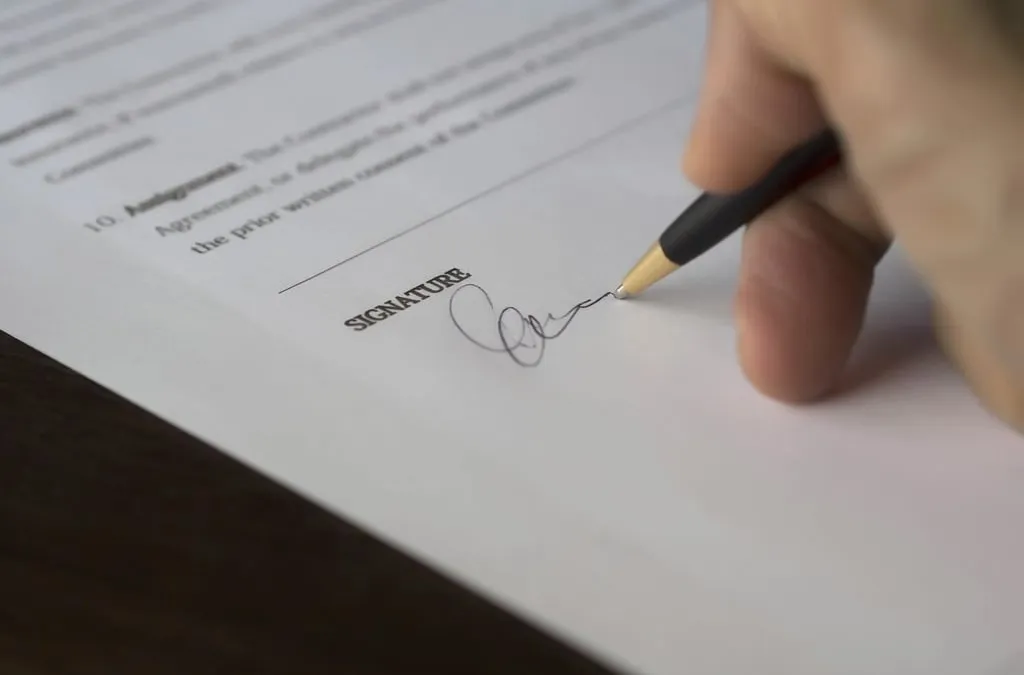 A hand signing a document with a pen