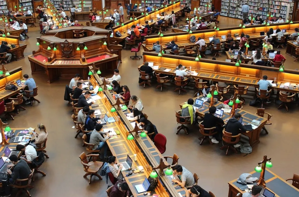 A large library reading room seen from above, with students at long desks under green lamps