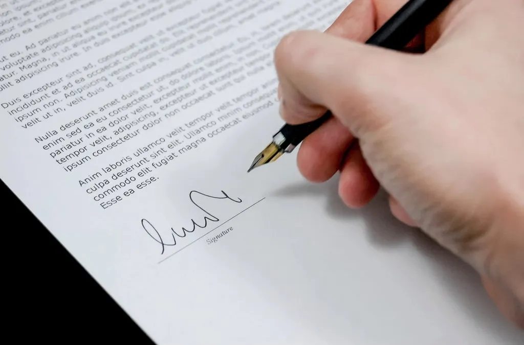 A hand signing a printed document with a fountain pen