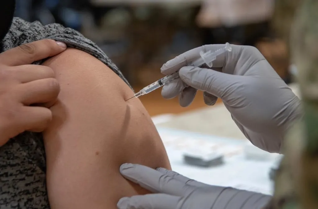 A gloved hand giving a vaccine injection in a person's upper arm