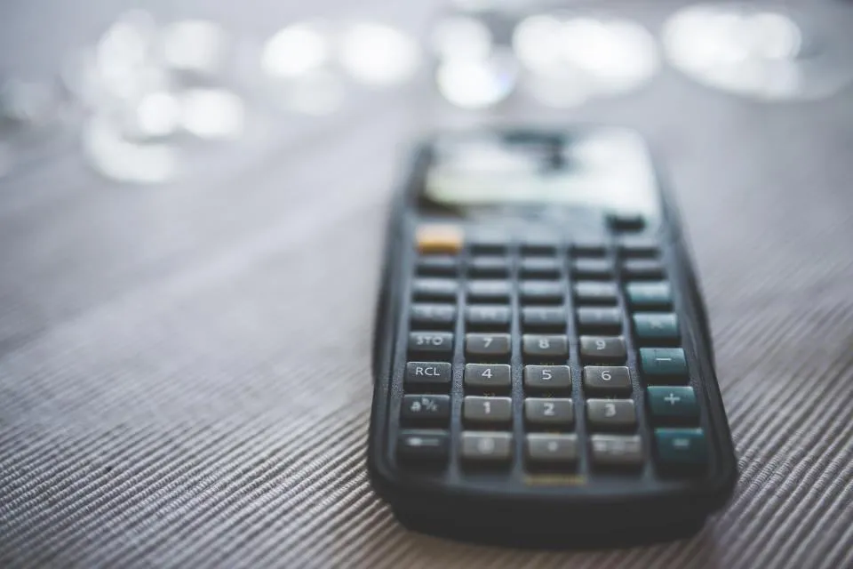 A black calculator standing on a gray textured cloth with soft blurred lights behind it