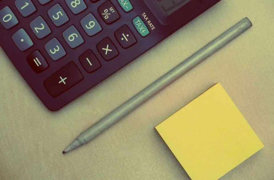 Close view of a calculator with a tax rate key, a gray pencil and a yellow sticky note